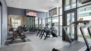 A modern gym with multiple exercise machines, large windows, and a TV displaying sports events. - Level - Fulton Market spacious 2 bedroom, 2 bath suite with full kitchen (Chicago)