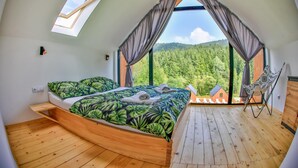 Une chambre à coucher avec un lit, un plancher en bois, une fenêtre avec des rideaux et une vue sur une forêt.