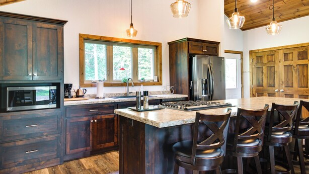 Una cucina moderna con mobili in legno scuro, una grande isola con sgabelli da bar, un frigorifero in acciaio inossidabile e illuminazione a sospensione.