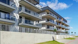 Ein modernes, mehrgeschossiges Wohngebäude mit Balkonen, einer Betonfassade und blauem Himmel.