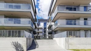 Ein modernes Apartmenthaus mit mehreren Balkonen, einer zentralen Treppe und blauem Himmel.