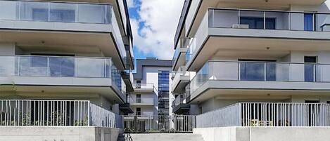 A modern apartment building with multiple balconies, a central staircase, and a clear sky.