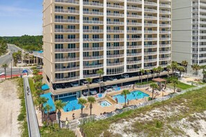 Ein mehrstöckiges Hotel mit Poolbereich auf dem Dach, einschließlich eines kleineren Pools und einer Strandlounge mit Sonnenschirmen.