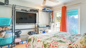 A room with bunk beds, a TV, a fan, and a window with curtains. - Surfer's Paradise: Waialua Condo Steps to Beach! (Waialua)