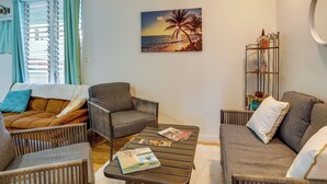 A living room with a sofa, two armchairs, a coffee table, and a painting of a beach scene. - Surfer's Paradise: Waialua Condo Steps to Beach! (Waialua)