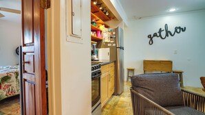 A compact kitchen with wooden cabinets, a built-in oven, and a refrigerator. A 'gather' sign is visible on the wall. - Surfer's Paradise: Waialua Condo Steps to Beach! (Waialua)