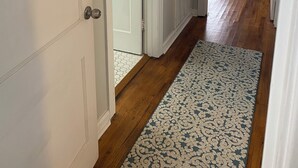 Un pasillo con puertas blancas, un tapete estampado y una estantería al fondo.