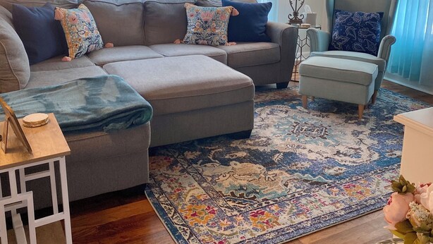 Una sala de estar acogedora con un sofá modular, una mesita auxiliar, un sillón decorativo y una alfombra estampada.