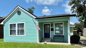 Una casa pequeña de un piso con fachada azul, un porche y una bandera.