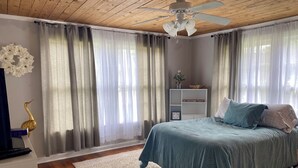 Un dormitorio con cama, ventilador de techo, mesita de noche y ventana con cortinas.