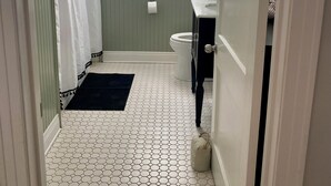 Un baño con piso de baldosas hexagonales, inodoro blanco, lavamanos y ventana con cortinas.