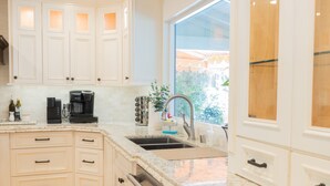 Una cocina con armarios blancos, un lavamanos de acero inoxidable y una ventana con vistas a zonas verdes.