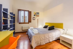 Quarto com cama, mesa de cabeceira, abajur e janela.