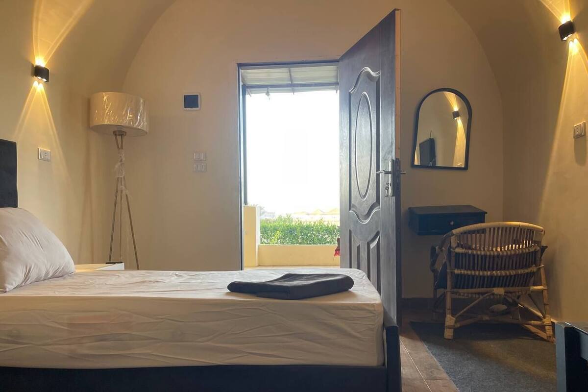 A bedroom with a bed, a chair, a lamp, and a view through an open door.