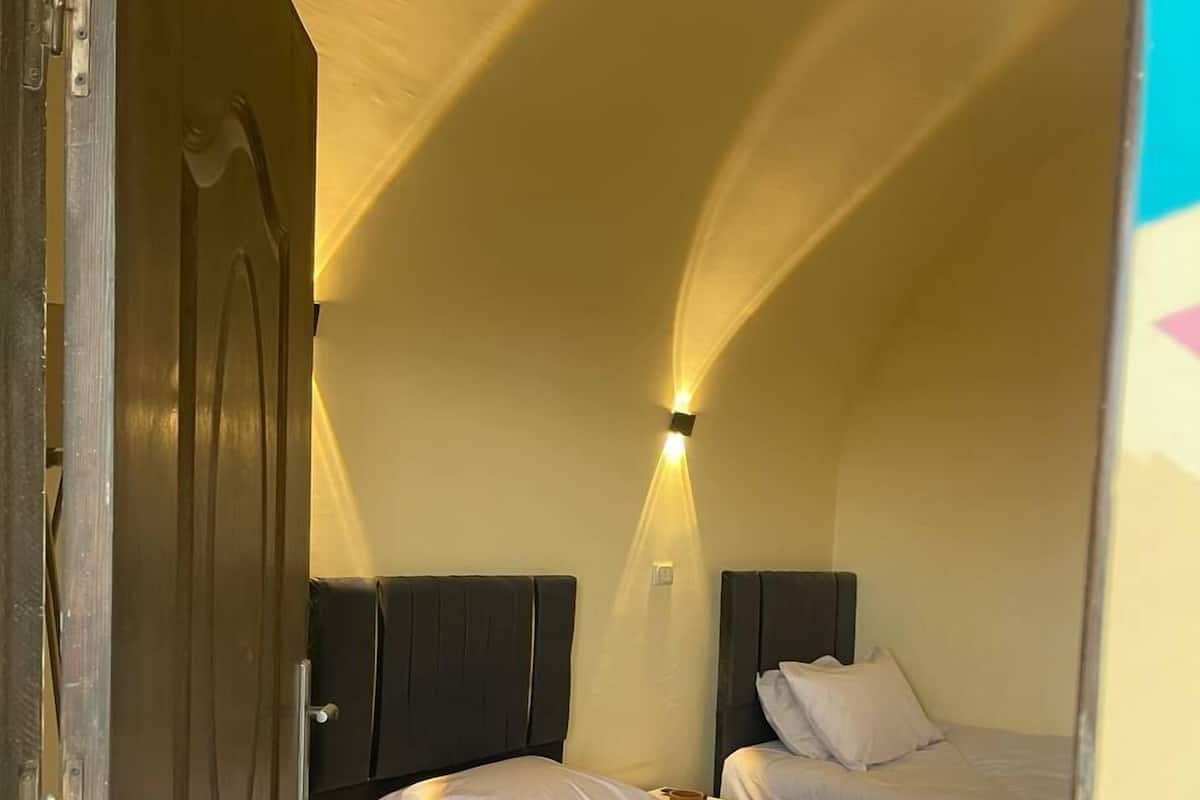 A compact bedroom with two beds, a small bedside table, and a wall-mounted light fixture.