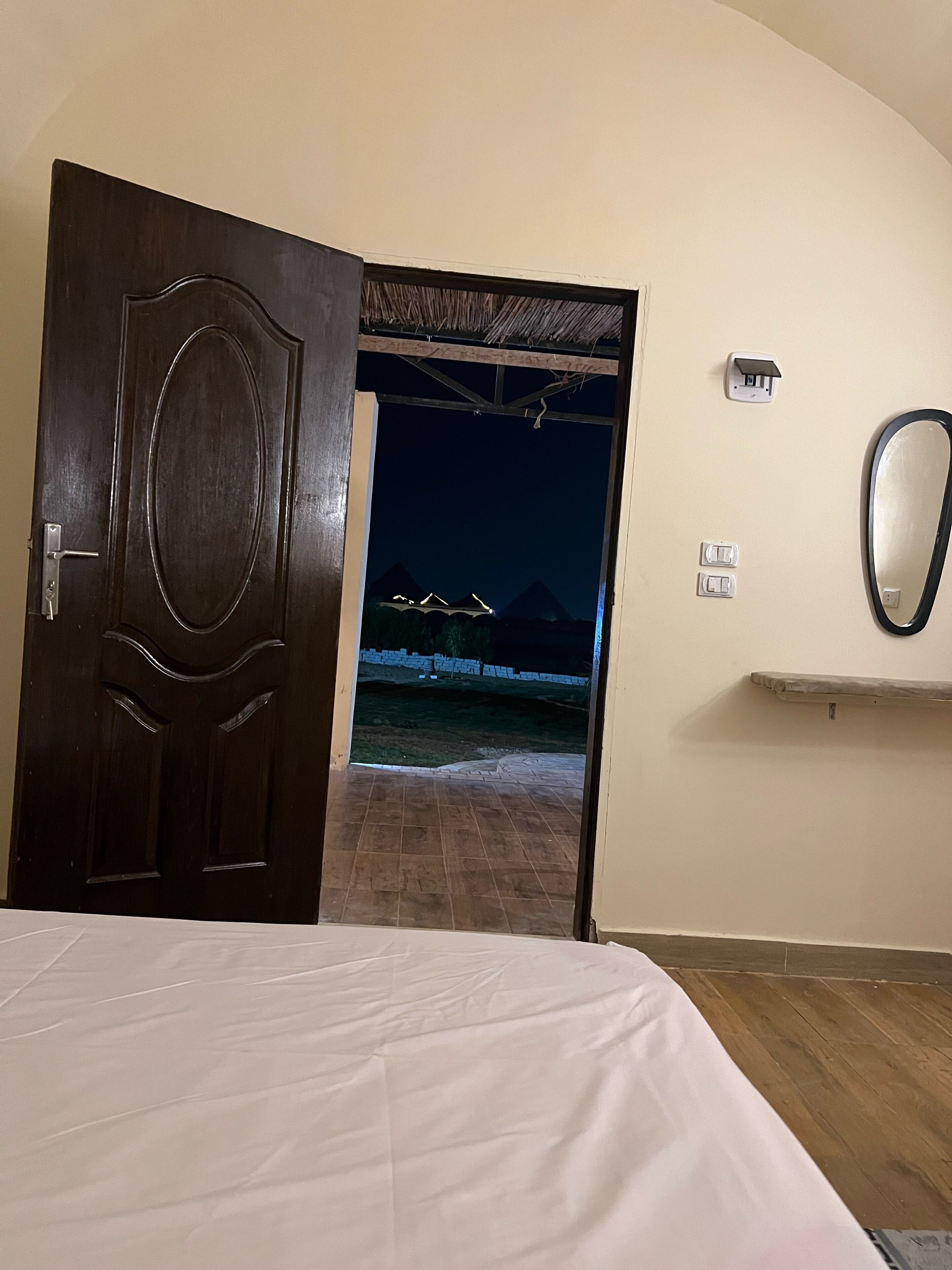 Habitación de hotel con puerta de madera que da a un balcón con vistas a montañas y un puente, de noche.