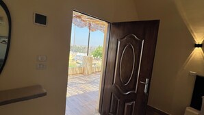 Una habitación con puerta de madera, un estante pequeño, una cama y vista a un área exterior con mesa y sombrilla.