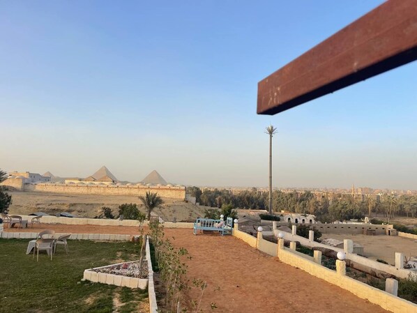 A view of a desert landscape with pyramids in the distance, a fenced area with a bench, and a tall pole. - Camp Pyramids View Hotel (Kirdasah)
