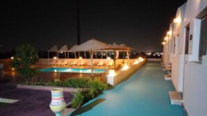 Un área junto a la piscina con sillones de descanso y una zona de estar techada de noche.