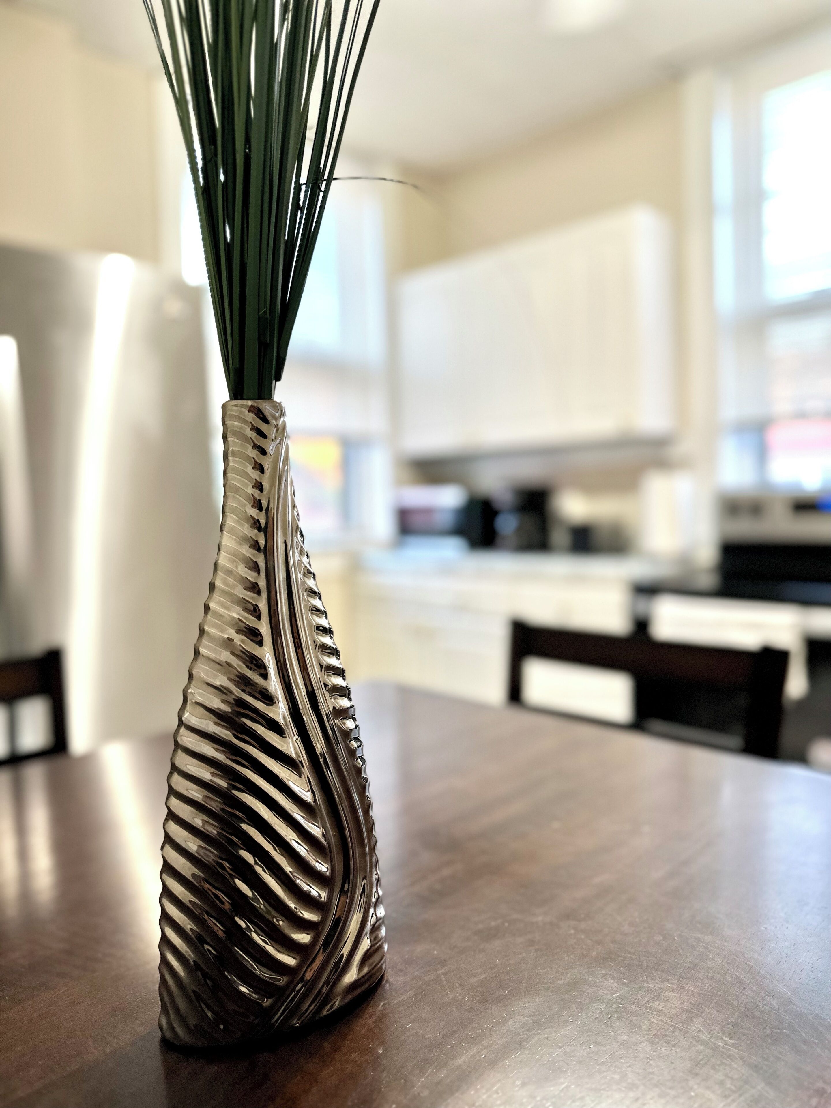 Un florero con diseño texturizado sobre una mesa de madera en una cocina con armarios y una ventana.
