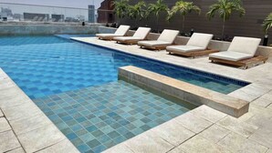 Une piscine sur le toit, avec un sol carrelé, des chaises longues et des palmiers.