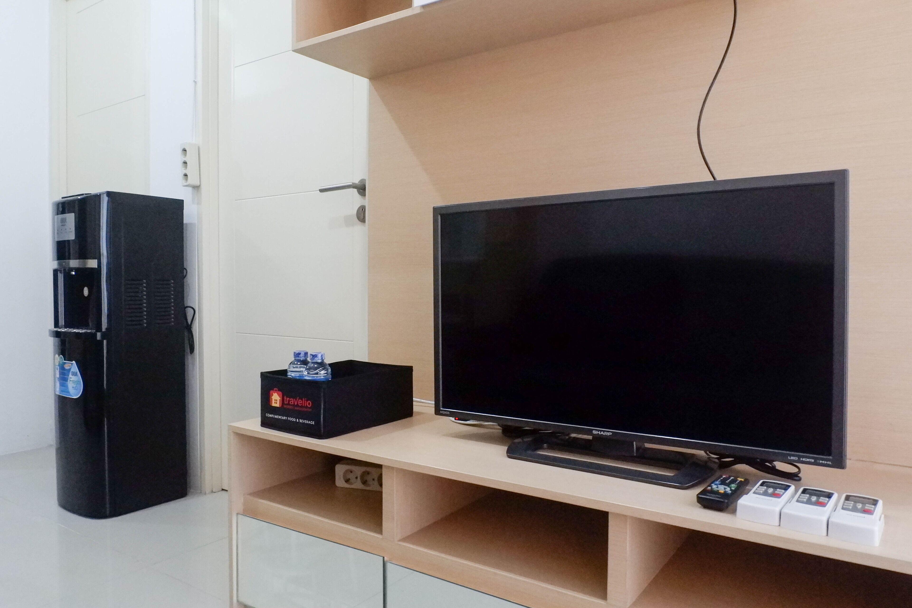 A modern room with a flat-screen TV on a wooden stand, a black refrigerator, and a travel box on the stand.