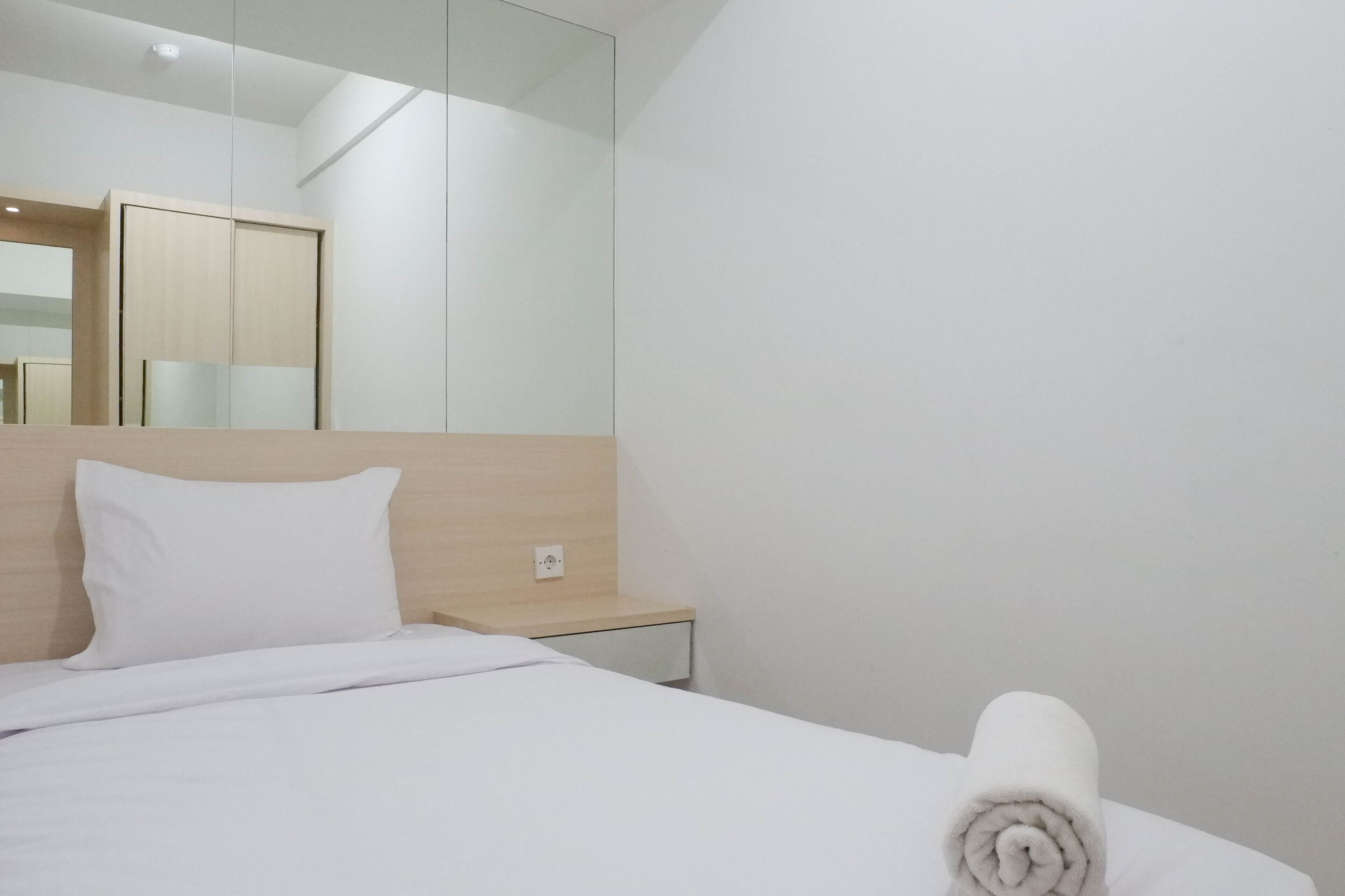 A hotel room with a bed, a nightstand, a mirror, and a wooden headboard.