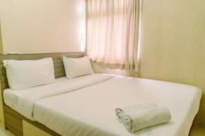 A neatly made bed with white linens and a rolled towel, a wooden headboard, and sheer curtains. - Comfort And Simply 2Br At Green Pramuka City Apartment (Jakarta)