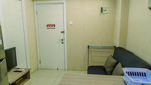 A small room with a sofa, a table, a television on a stand, and a door with a fire exit sign. - Comfort And Simply 2Br At Green Pramuka City Apartment (Jakarta)
