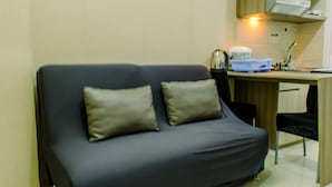 A small, dark-colored sofa with two cushions in a compact room with a kitchenette area. - Comfort And Simply 2Br At Green Pramuka City Apartment (Jakarta)