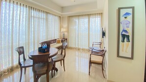 A hotel dining area with a round table, chairs, and a bench. There is a painting on the wall and a lamp on a side table. - Nice And Homey 2Br Apartment At Menteng Park (Jakarta)