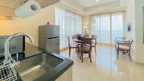 A modern kitchen with a stainless steel sink, a refrigerator, and a dining area with wooden chairs and a table. - Nice And Homey 2Br Apartment At Menteng Park (Jakarta)