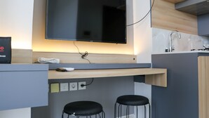A modern kitchen with a flat-screen TV mounted above a wooden countertop, a built-in sink, and two black bar stools. - Good Deal and Comfy Studio West Vista Apartment (Jakarta)