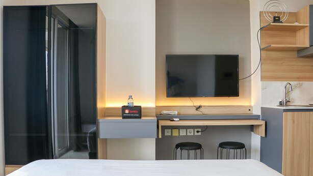 A modern hotel room with a bed, a desk with a computer, a TV, and a small kitchen area. - Good Deal and Comfy Studio West Vista Apartment (Jakarta)