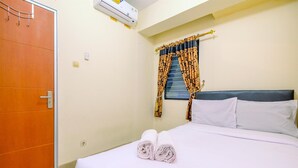 A hotel room with a bed, a window with patterned curtains, an air conditioning unit, and a door. - Comfort And Cozy Living 2Br At Cibubur Village Apartment (Depok)