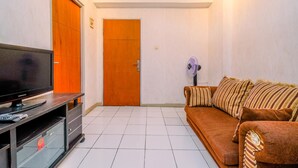 A living room with a television on a stand, a sofa, a wooden door, and a fan. - Comfort And Cozy Living 2Br At Cibubur Village Apartment (Depok)