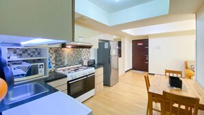 Una cocina compacta con estufa a gas, microondas y electrodomésticos modernos. Cuenta con un comedor con mesa y sillas de madera. La cocina tiene un salpicadero de azulejos y armarios de color claro.