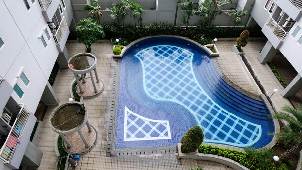 An aerial view of a residential building with a swimming pool, surrounded by greenery and a tiled walkway. - Cozy Living And Tidy 2Br At Puncak Dharmahusada Apartment (Surabaya)