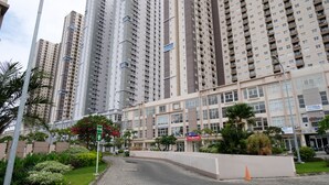 A high-rise residential building with multiple balconies, a gated entrance, and commercial establishments including a laundry service. - Cozy Living And Tidy 2Br At Puncak Dharmahusada Apartment (Surabaya)