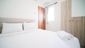 A neatly made bed with white linens, a wooden wardrobe, and a window with curtains. - Cozy Living And Tidy 2Br At Puncak Dharmahusada Apartment (Surabaya)