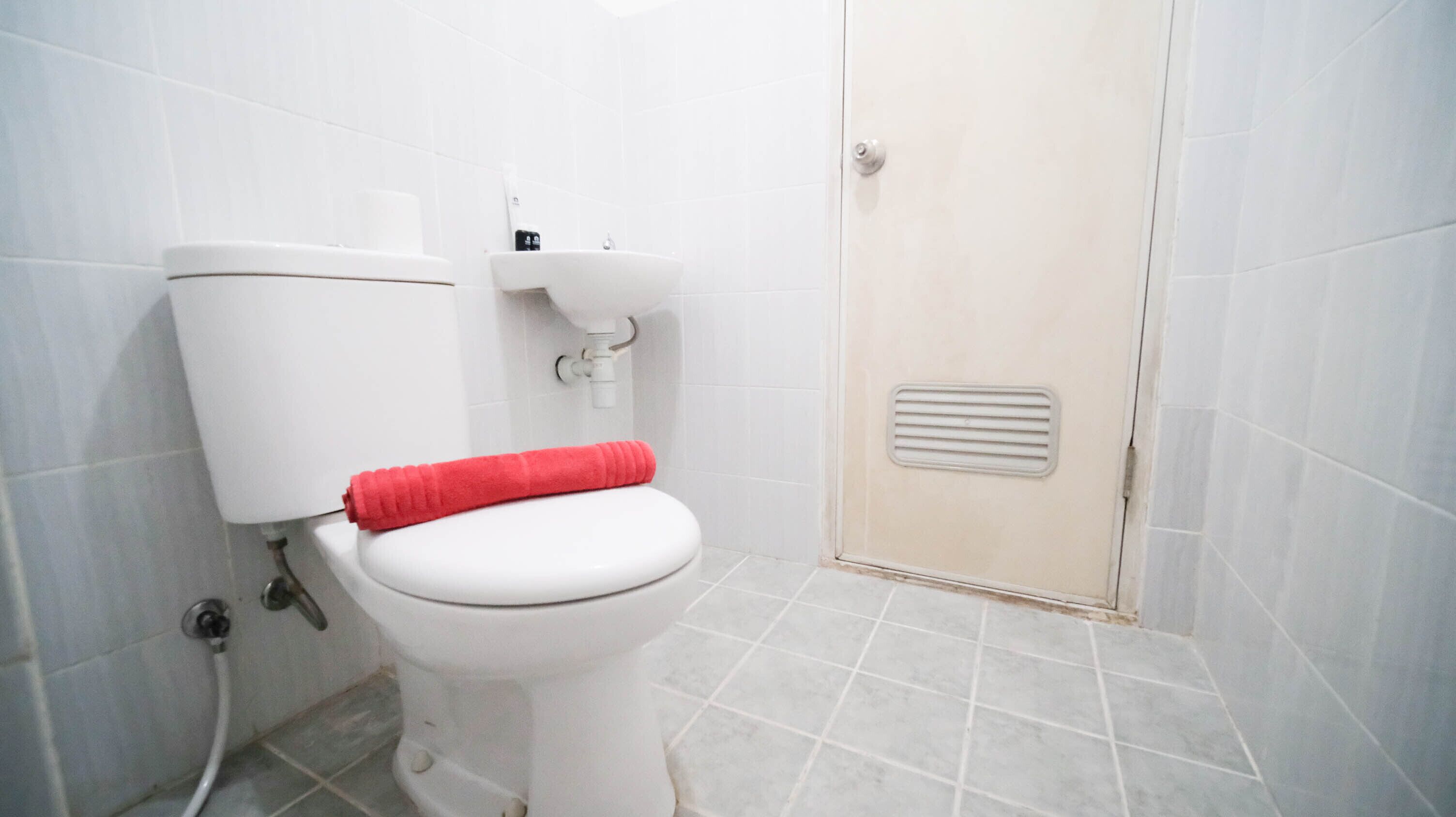 A white toilet with a red towel, a sink, and a shower door in a bathroom with tiled walls and floor.