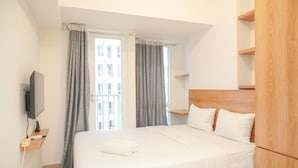 A hotel room with a bed, a TV, a wooden headboard, and a window with curtains.