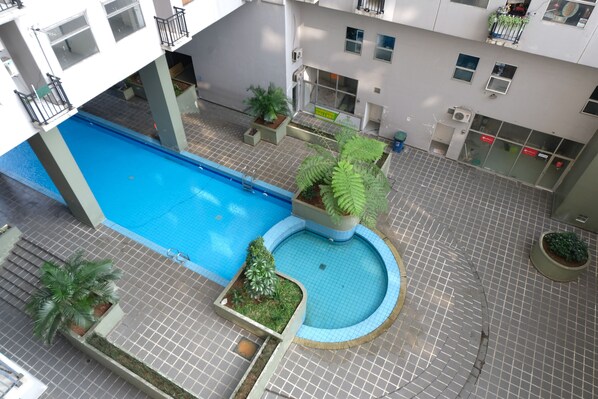 Un espace piscine aménagé sur le toit, avec une piscine bleue, entourée de plantes en pot et dotée d’un sol carrelé.