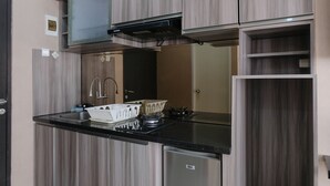 A compact kitchen with a built-in gas stove, a sink, and a compact refrigerator. - Spacious Studio With Extra Room At Grand Asia Afrika Apartment (Bandung)