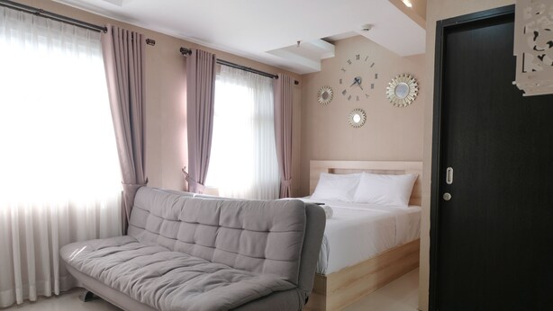 A modern bedroom with a sofa, a bed, and decorative wall clocks. - Spacious Studio With Extra Room At Grand Asia Afrika Apartment (Bandung)
