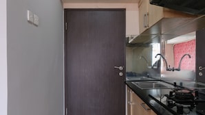 A kitchen with a dark wooden door, stainless steel appliances, and a sink. - Good Deal 2Br Apartment At Jarrdin Cihampelas (Bandung)