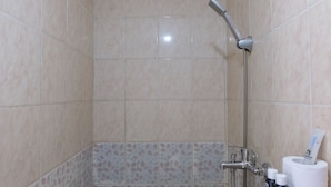 A bathroom with beige tiles, a showerhead, a toilet paper holder, and two bottles of toiletries. - Good Deal 2Br Apartment At Jarrdin Cihampelas (Bandung)