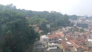 A densely packed urban area with traditional buildings and a forested hill in the background. - Good Deal 2Br Apartment At Jarrdin Cihampelas (Bandung)
