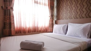 A neatly made bed with white linens and a folded towel, a headboard with a wavy pattern, and sheer curtains with a light filter. - Good Deal 2Br Apartment At Jarrdin Cihampelas (Bandung)