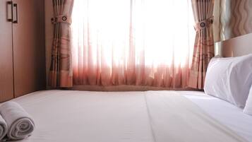 A hotel room with a large bed, a wooden wardrobe, and sheer curtains.